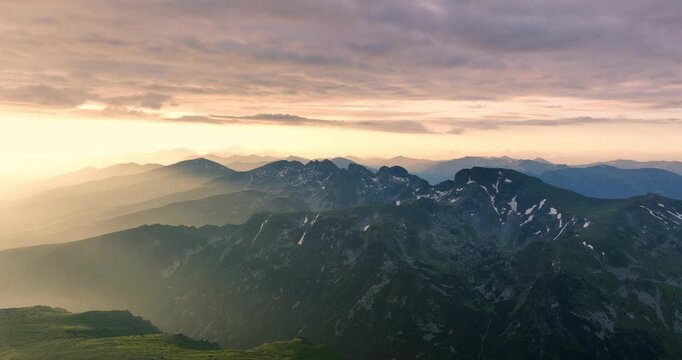 Panoramic view at sunrise over mountain peaks of Rila National Park and Seven rila lakes. Golden sun rays through dramatic clouds over green slopes in Bulgaria