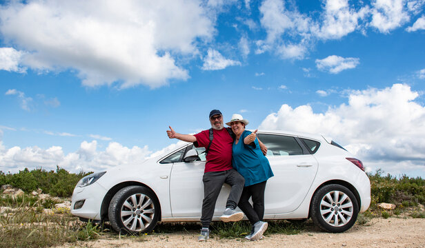 Pareja de jubilados al lado de su coche en la monta&ntilde;a un d&iacute;a soleado con nubes.