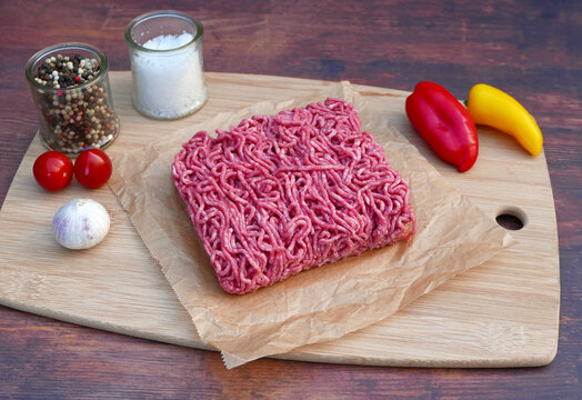 Fresh minced meat on a wooden board with peppers, tomatoes and spices.