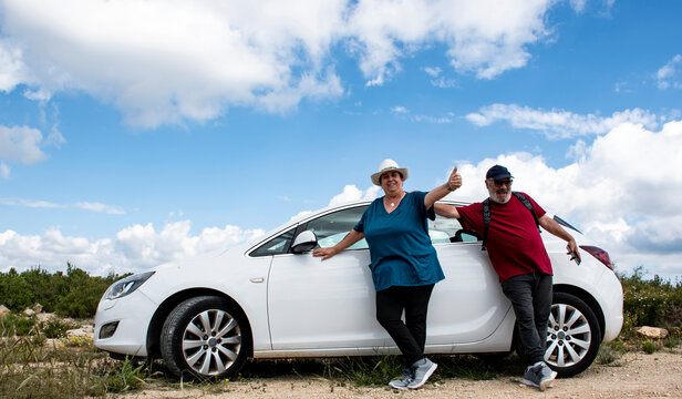 Pareja de jubilados al lado de su coche en la monta&ntilde;a un d&iacute;a soleado con nubes.