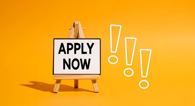 Small wooden easel stands proudly displaying a white board with the bold black text apply now accompanied by three bright white exclamation marks isolated against a vibrant solid yellow background