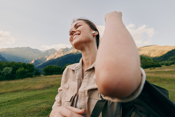 Fototapeta premium Cheerful woman outdoors, smiling, backpack ready, nature surrounds a scenic field with distant mountains, daylight glow, casual style, relaxed pose, joyful moment in open landscape