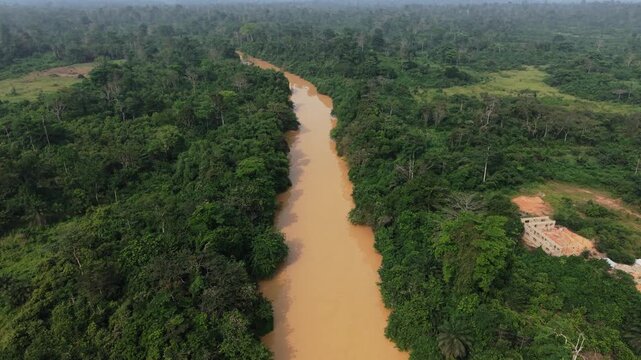 Brown, muddy river flowing through a deforested landscape, showing environmental destruction from illegal mining