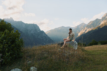 Naklejka premium A woman sits on a rock in a mountain meadow, enjoying the view, calm and reflective. A nature driven moment that conveys outdoor lifestyle and solo exploration.