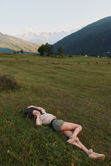 Fototapeta premium Cheerful woman lying in a grassy meadow outdoors, sunlit mountains in the background, relaxed pose, gentle breeze, natural colors, carefree lifestyle in bright daylight