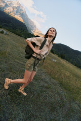 Fototapeta premium A woman on a sunny hillside enjoys hiking, outdoors, and travel with a backpack, embodying adventure in a vast mountain landscape, clear sky, and peaceful nature.