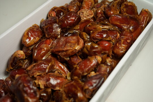 High angle shot of sweet dried dates packed in a white box. The dates have a glossy texture and rich brown color, perfect for healthy snack or Ramadan food concepts.