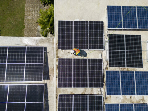 Aerial view of a technician installing solar panels on a rooftop with lush greenery nearby in Guanaja, Bay Islands Department, Honduras.