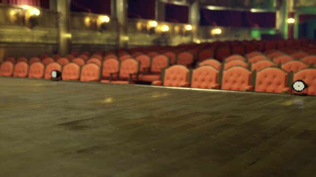 Empty stage with red velvet seats, polished wooden floor and dimmed spotlight ornate balcony and rows receding into silent auditorium, preshow stillness evokes