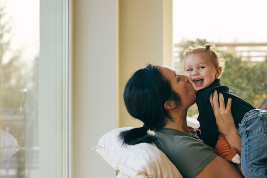 Affectionate mother kissing daughter while spending leisure time at home