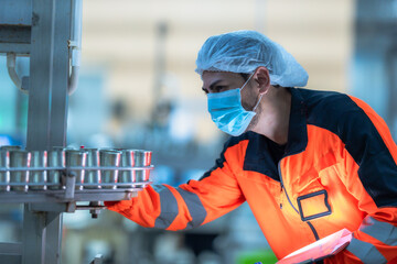 Fototapeta premium A focused technician in a bright safety uniform and mask inspecting an automated conveyor system during a shift in a modern manufacturing plant.