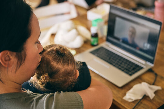 High angle view of mother kissing daughter having fever while listening to doctor's advice through video call at home