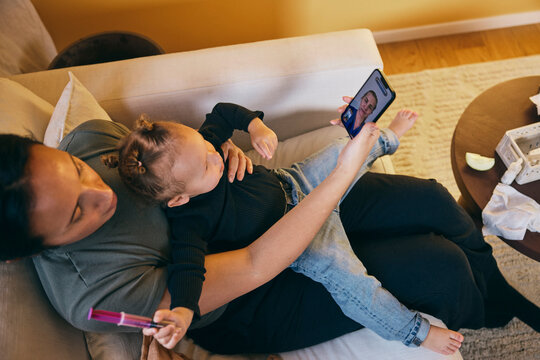High angle view of woman talking with female doctor advising on daughter's fever problems through video call in home