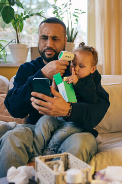Father checking body temperature of daughter through thermometer while talking with doctor on video call at home