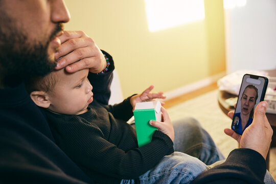 Father explaining daughter's body temperature due to fever to female pediatrician on video call through smart phone at h
