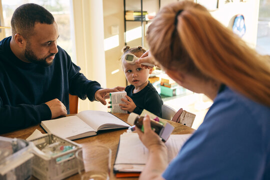 Female pediatrician checking body temperature of girl through thermometer during home visit