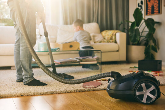Low section of man cleaning carpet with vacuum cleaner in living room at home
