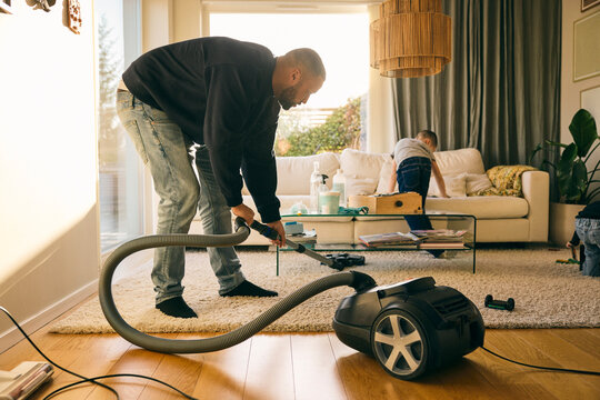 Full length of man cleaning carpet under tea table in living room at home
