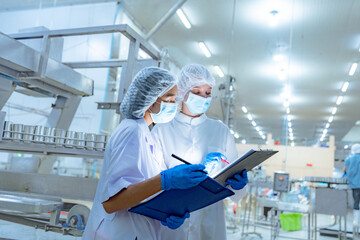 Naklejka premium Workers in safety gear inside a factory check equipment and products on production and transportation lines in a closely monitored, state-of-the-art food processing plant.