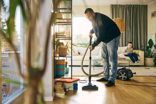 Full length of man cleaning floor of living room with vacuum cleaner at home