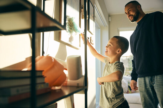 Smiling elementary boy cleaning picture frame with duster while helping father in home