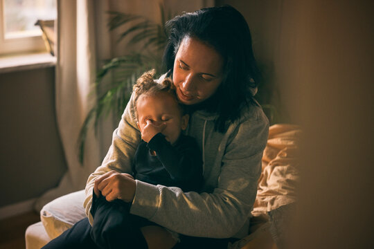 Mother sitting with sleepy daughter in bedroom at home