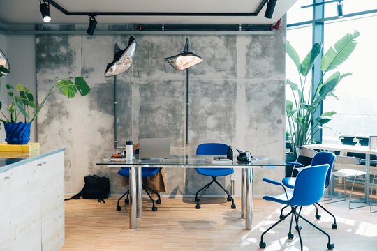 Modern office interior with blue chairs and glass desk against gray concrete wall