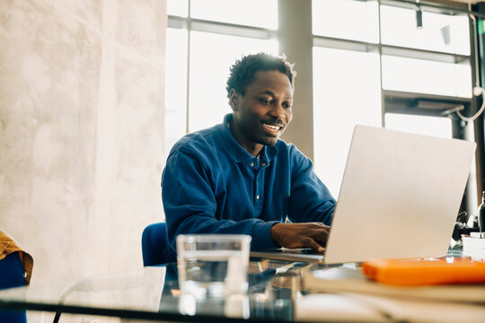 Smiling male computer programmer working on laptop while sitting at desk in office