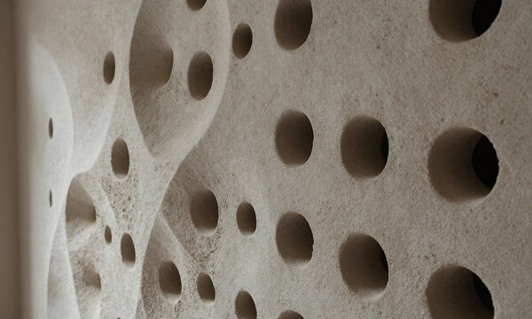 textured undulating wall numerous circular voids irregular crevices partially lit soft diffused natural light