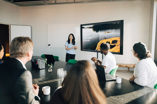 Group of colleagues listening to presentation from young female employee at modern startup office