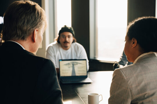 Rear view of male and female investors sitting with team in modern meeting room at office