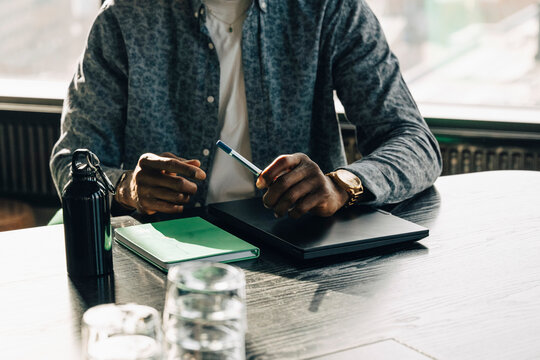 Midsection of businessman sitting with laptop and diary at table in meeting room