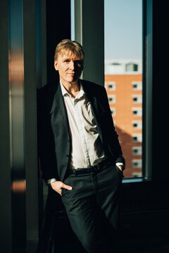 Portrait of confident businessman posing with hands in pockets while leaning on office wall