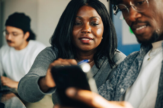 Coworkers looking at smart phone screen together at modern office