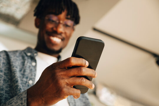 Low angle view of smiling businessman scrolling smart phone during coffee break at office