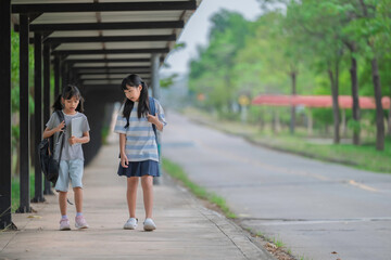 Obraz premium Happy Asian student girls with backpacks walking and running together at school. Back to school concept with kids smiling and having fun outdoors while going to classroom for education and learning.