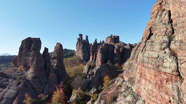 Medium-close aerial pass through natural rock formations rising above colorful autumn woodland.