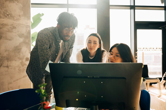 Group of computer programmers looking at monitor screen while working at modern startup office