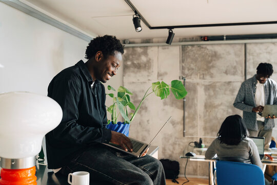 Smiling computer programmer working on laptop while sitting in modern startup office