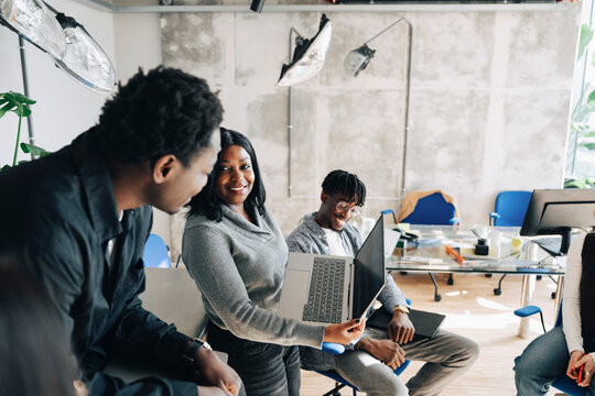 Smiling businesswoman sharing laptop with male colleague at modern startup office