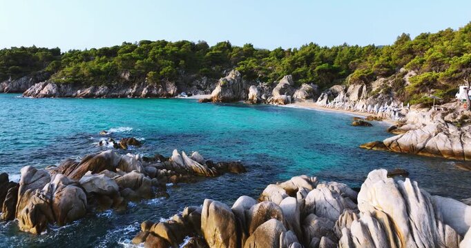 Hidden beach with rocks lush green pine trees in Halkidiki, Greece. Crystal clear turquoise sea water washing the shore.