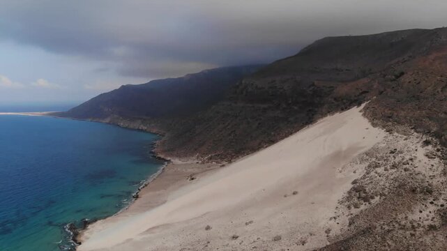 Aerial flight over a red rock formation on the coast of socotra island by the blue ocean, perfect for exotic travel documentaries, nature exploration videos or alien landscape backgrounds