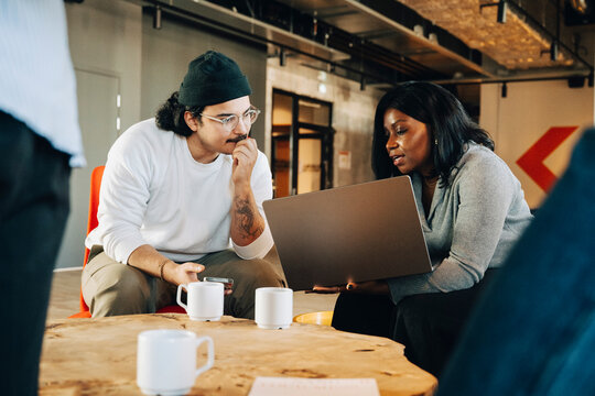 Businesswoman sharing business idea with male colleague over laptop while sitting at startup workspace