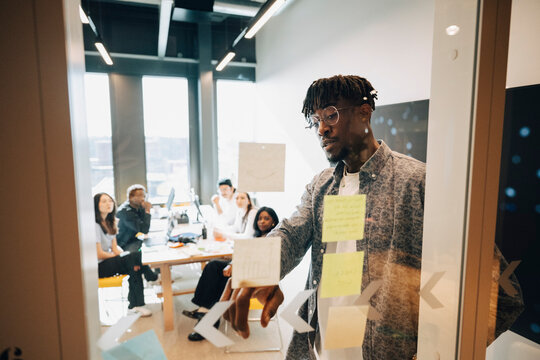 Businessman pointing at notes on glass wall during team presentation at modern startup office