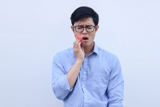 close up young asian man frown and use hand to massage on cheek after feeling pain or hurt from tmj muscle symptom at home for un healthy lifestyle and treatment concept