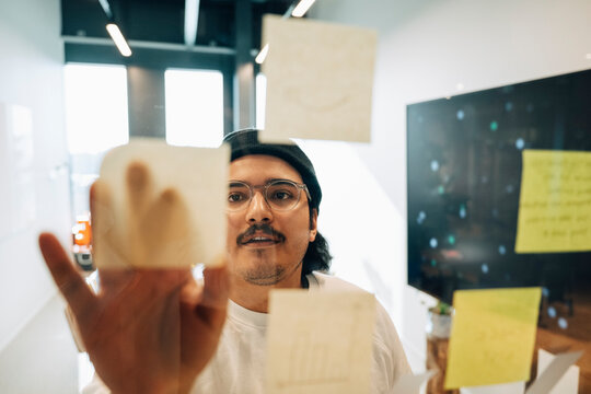 Young male business professional sticking adhesive notes on glass wall at office