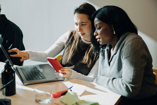 Female programmers multi-tasking with wireless technologies while working at modern startup office