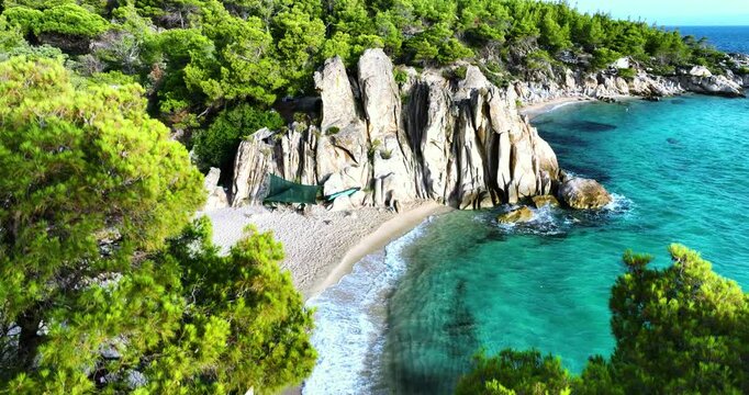 Hidden beach with rocks lush green pine trees in Halkidiki, Greece. Crystal clear turquoise sea water washing the shore.