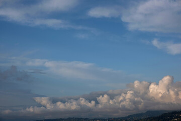 Obraz premium Fluffy white clouds over a green mountain range and coastal town