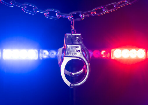 Police handcuffs hanging on a chain with red and blue lights flashing in the background during night hours in a law enforcement setting
